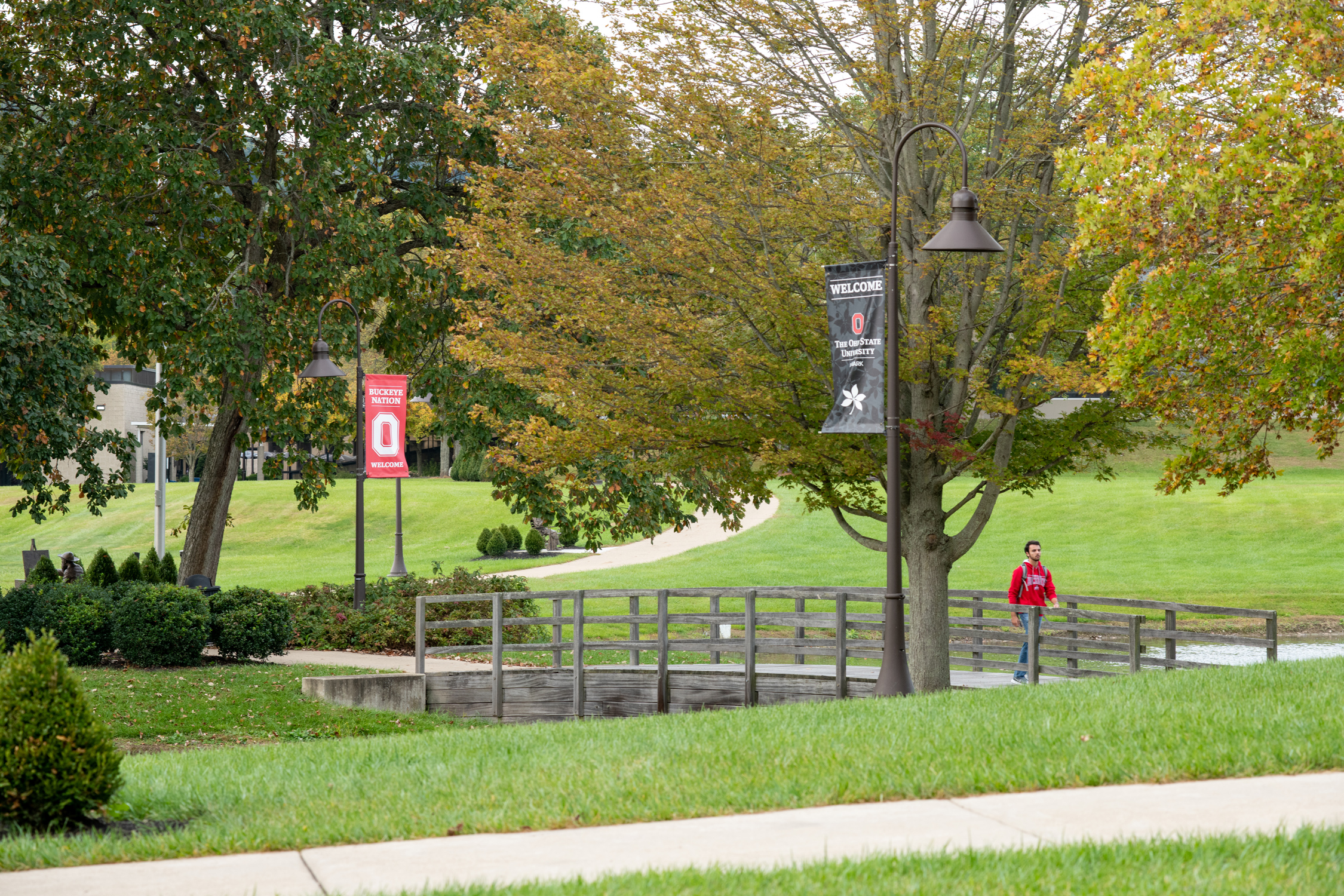 The Ohio State University Newark campus grounds. A student walks across a small pedestrian bridge