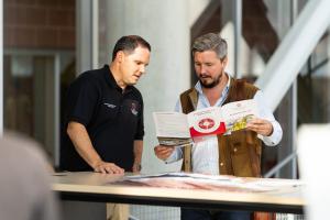 Two men are seen talking while one holds a Framework 3.0 pamphlet 